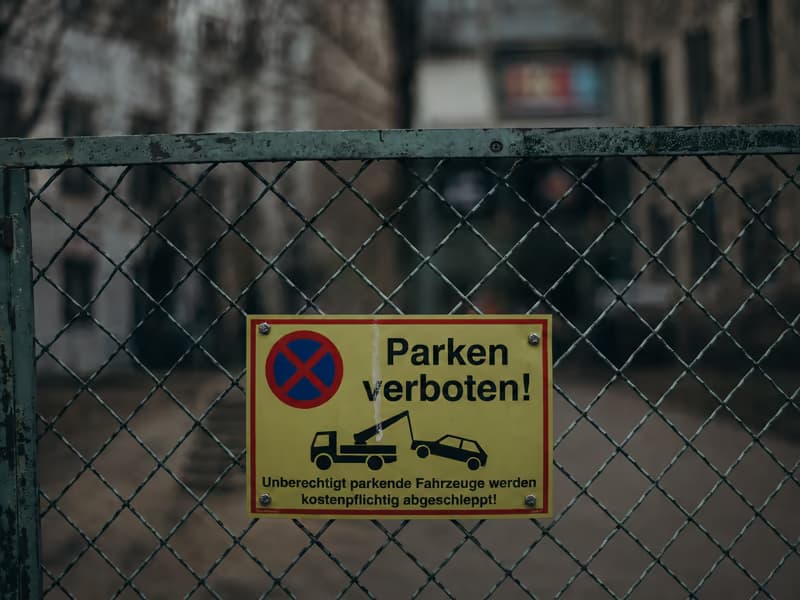 Gelbes Schild «Parken verboten» an einem Maschendrahtzaun: unberechtigt parkende Fahrzeuge werden kostenpflichtig abgeschleppt