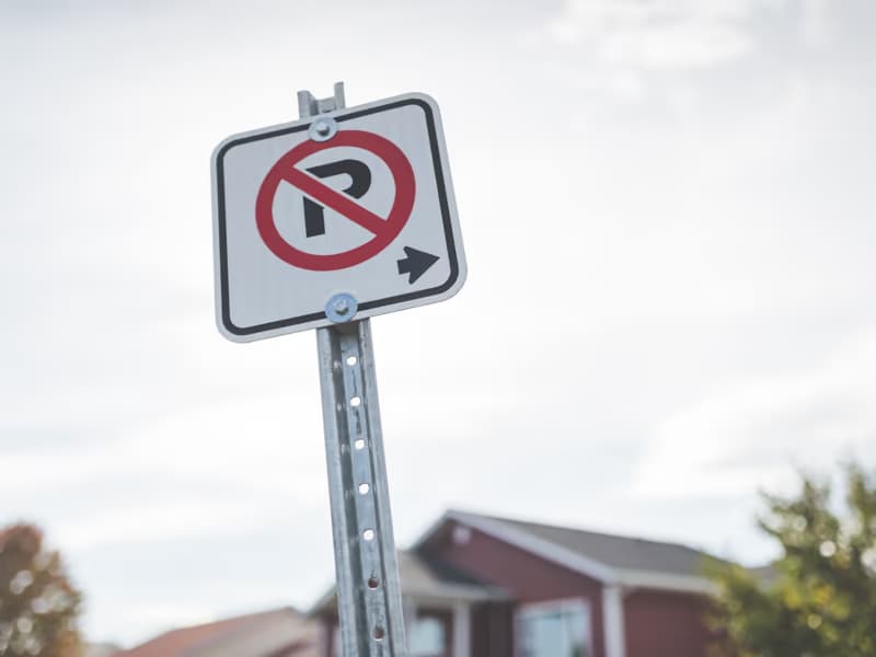 Parkverbotsschild mit Richtungspfeil an einem Pfosten vor bewölktem Himmel