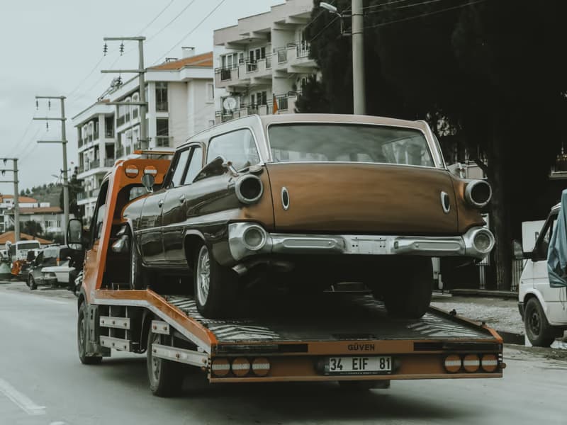 Brauner Oldtimer auf der Ladefläche eines Abschleppwagens in einer Stadtstrasse