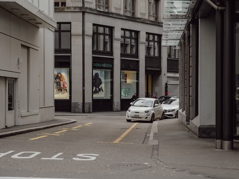 Weisses Auto an einer Strassenecke vor Schaufenstern in der Innenstadt