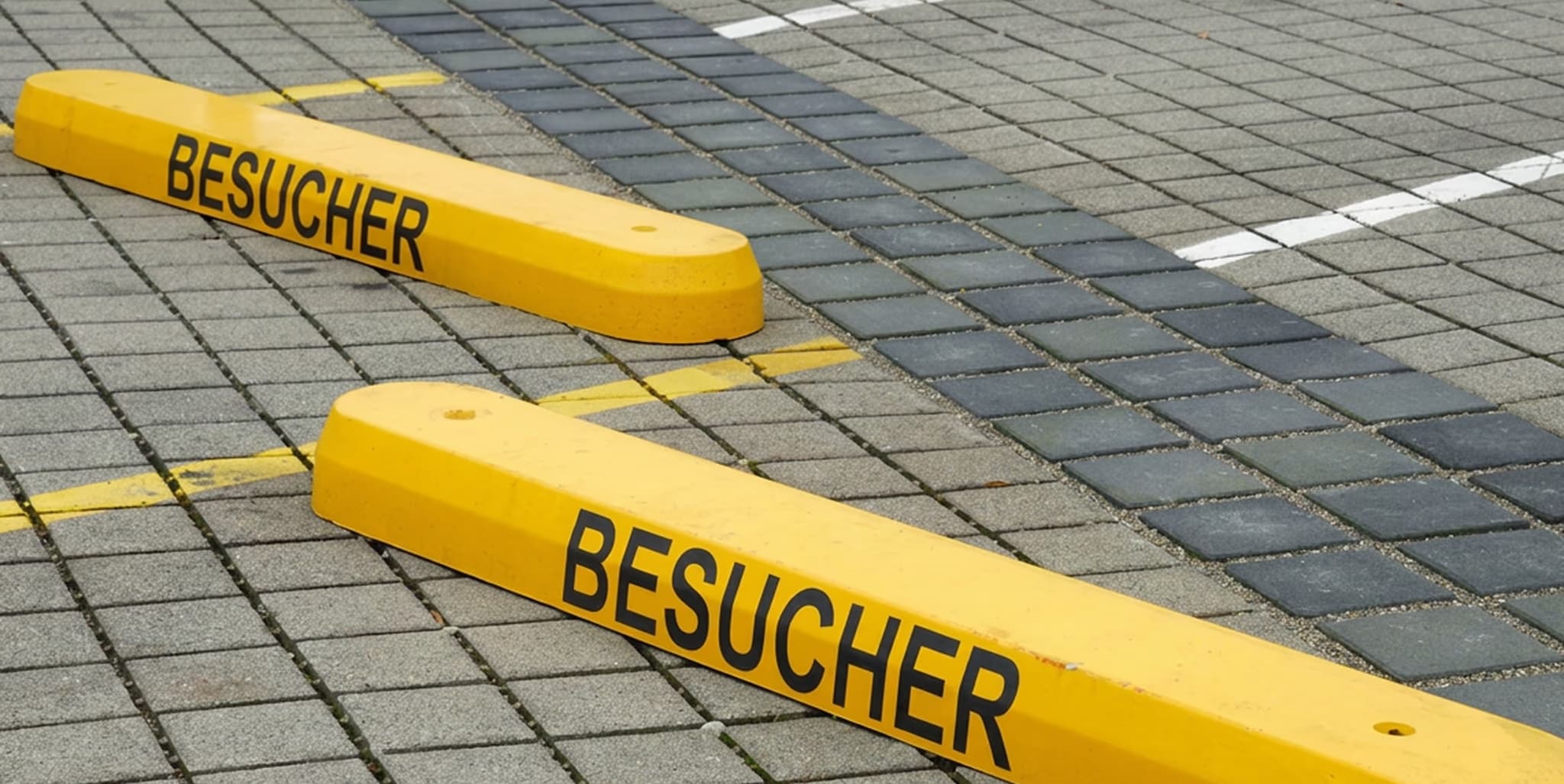 Zwei gelbe Parkbegrenzungen mit der Aufschrift «BESUCHER» auf einem gepflasterten Parkplatz